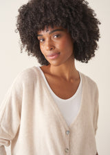 A woman wearing a light oatmeal cream knit cardigan over a white V-neck top and matching light oatmeal trousers.
