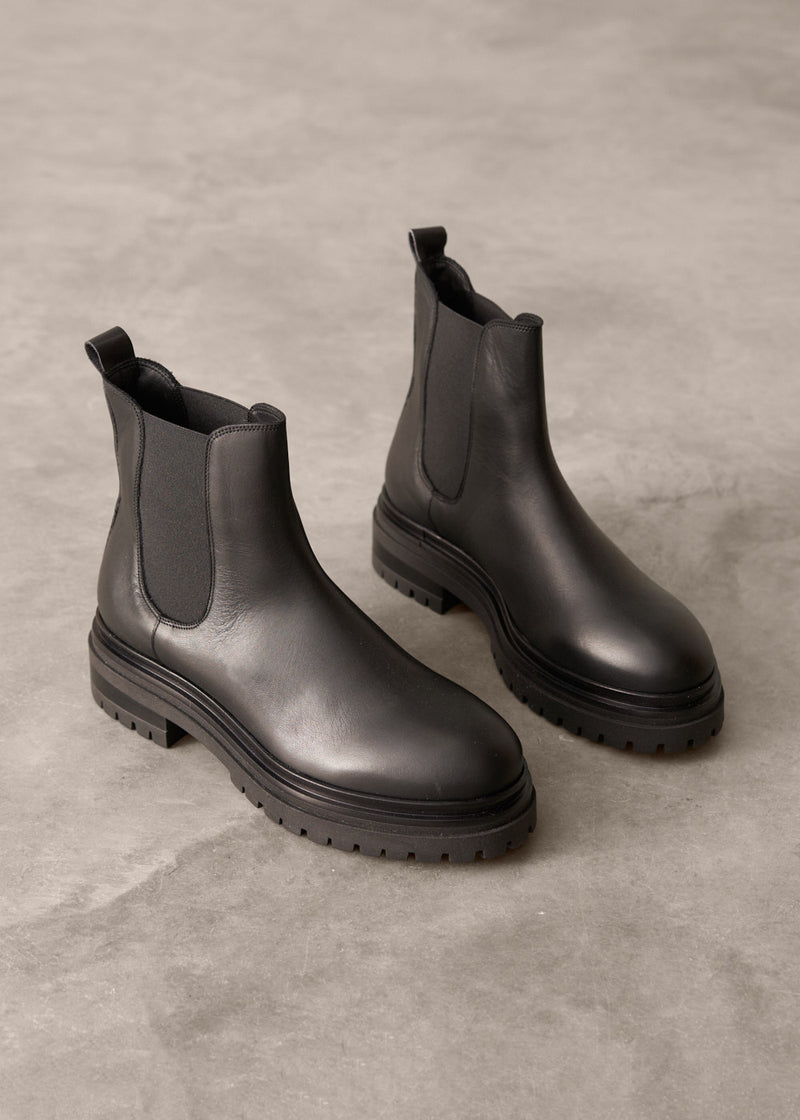 Pair of ankle length black leather Chelsea boots on a gray concrete surface