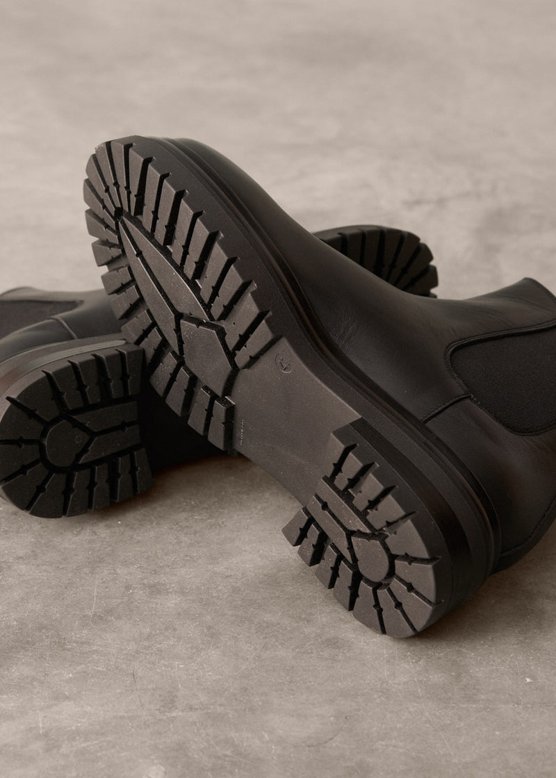 Close-up of black leather Chelsea boots with sole visible on a beige background