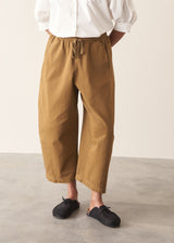 Woman wearing mustard yellow, olive green oversized barrel leg trousers with a white cotton shirt and black shoes.