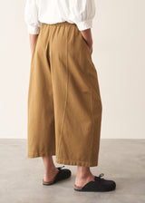 Woman wearing mustard yellow, olive green oversized barrel leg trousers with a white cotton shirt and black shoes.