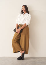 Woman wearing mustard yellow, olive green oversized barrel leg trousers with a white cotton shirt and black shoes.