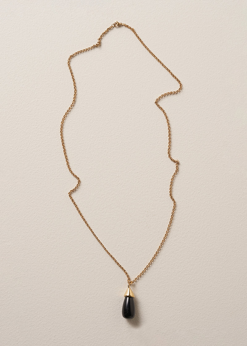 A long golden chain with a chunky black oval pendant, photographed against a simple beige background