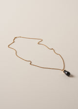 A long golden chain with a chunky black oval pendant, photographed against a simple beige background