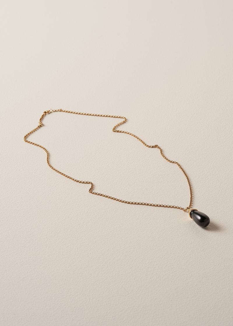 A long golden chain with a chunky black oval pendant, photographed against a simple beige background