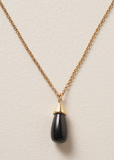 Close up of a long golden chain with a chunky black oval pendant, photographed against a simple beige background