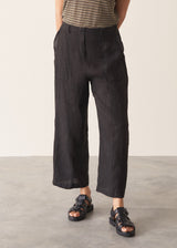 Woman wearing a striped t-shirt and black linen trousers, standing against a plain wall.