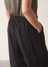 Woman wearing a striped t-shirt and black linen trousers, standing against a plain wall.