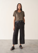 Woman wearing a striped t-shirt and black linen trousers, standing against a plain wall.