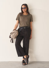 Woman wearing a striped t-shirt and black linen trousers, standing against a plain wall.