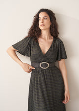 Woman wearing a dark patterned dress with a belt against a plain background