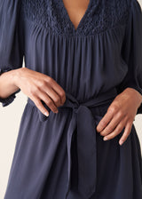 Close-up of a navy blue dress with a lace V-neck bodice, gathered waist, and self-tie belt, worn by a model.