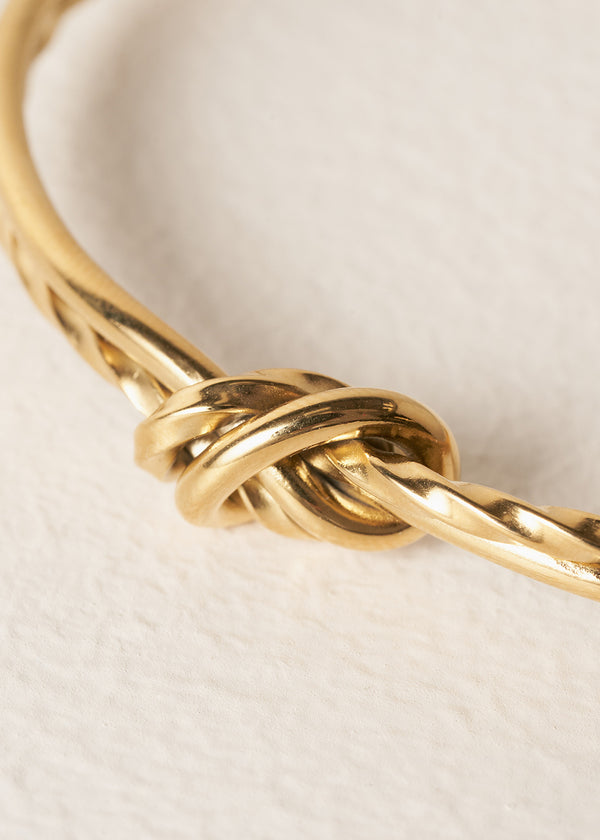 Gold bracelet with a knot design on a light beige background