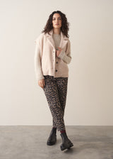 Woman wearing a beige boucle gilet over with leopard print trousers and chunky boots