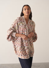 Woman wearing a multicoloured oversized cardigan and jeans  against a plain background