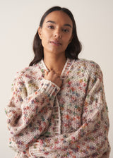 Woman wearing a multicoloured oversized cardigan and jeans  against a plain background