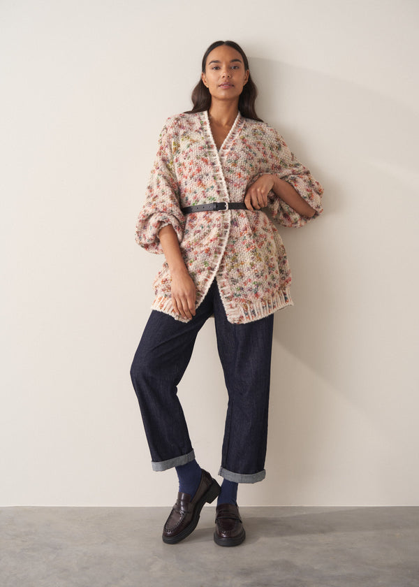 Woman wearing a multicoloured oversized cardigan and jeans  against a plain background