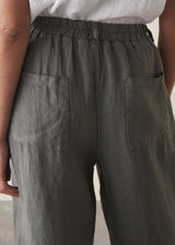 Woman wears a white linen shirst and matching cropped linen barrel-leg trousers against a beige background