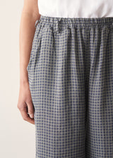 Woman wearing blue and green checked linen barrel leg trousers and a white top.