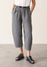 Woman wearing blue and green checked linen barrel leg trousers and a white top.