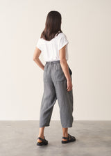 Woman wearing blue and green checked linen barrel leg trousers and a white top.
