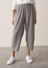 Woman wearing cotton seersucker checked barrel leg trousers and a white top.