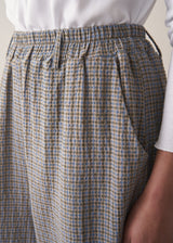 Woman wearing cotton seersucker checked barrel leg trousers and a white top.