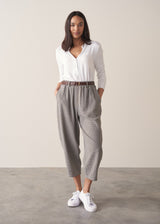 Woman wearing cotton seersucker checked barrel leg trousers and a white top.