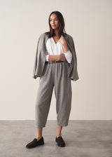 A woman models a blue-green checked cotton jacket over a white top, paired with matching barrel-leg trousers and brown loafers, set against a beige background