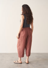 Woman wearing a sleeveless top and rust-coloured, cropped barrel-leg trousers against a plain background