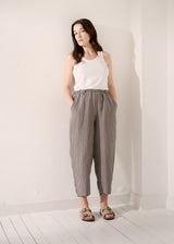 Woman wearing grey checked cropped linen barrel leg trousers and matching grey checked linen jacket with a white vest top