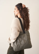 Woman carrying a quilted green bag on a plain background