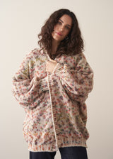 Woman wearing a space dye patterned oversized cardigan and blue jeans against a plain background