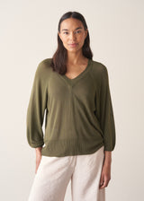 Woman wearing olive green v-neck sweater and pale trousers