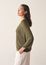 Woman wearing olive green v-neck sweater and pale trousers