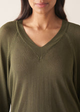 Woman wearing olive green v-neck sweater and pale trousers