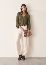 Woman wearing olive green v-neck sweater and pale trousers
