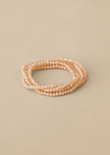 Long nude beaded necklace, styled as a bracelet, on beige background