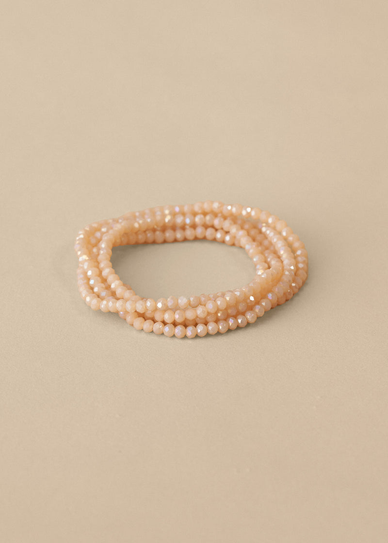 Long nude beaded necklace, styled as a bracelet, on beige background