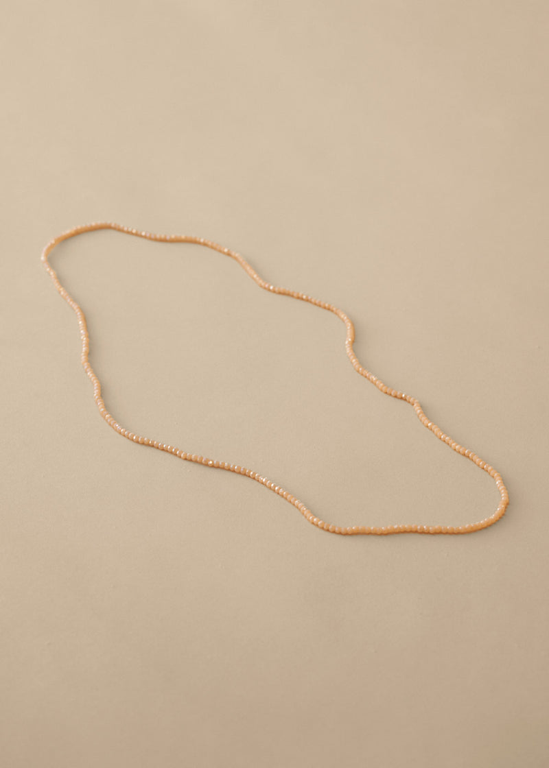 Long nude beaded necklace on beige background
