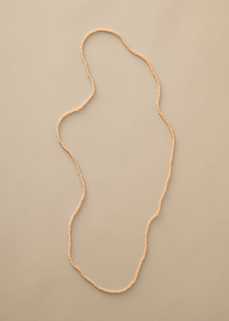 Long nude beaded necklace on beige background