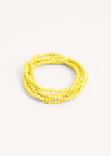 A long yellow crystal necklace styled as a bracelet on beige background