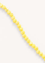 Close up of a long yellow crystal necklace on beige background