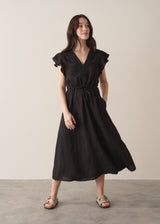 Woman wearing a black linen midi dress with a drawstring waist and embroidery detail on a beige background