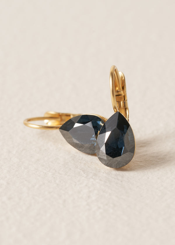 Pair of gold tear drop earrings with black crystal, on a beige background