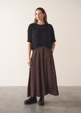 Woman wearing a black sparkle knit short sleeve sweater, leopard print skirt and black leather boots on a plain background