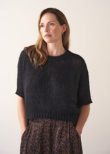 Woman wearing a black sparkle knit short sleeve sweater and a leopard print skirt on a plain background