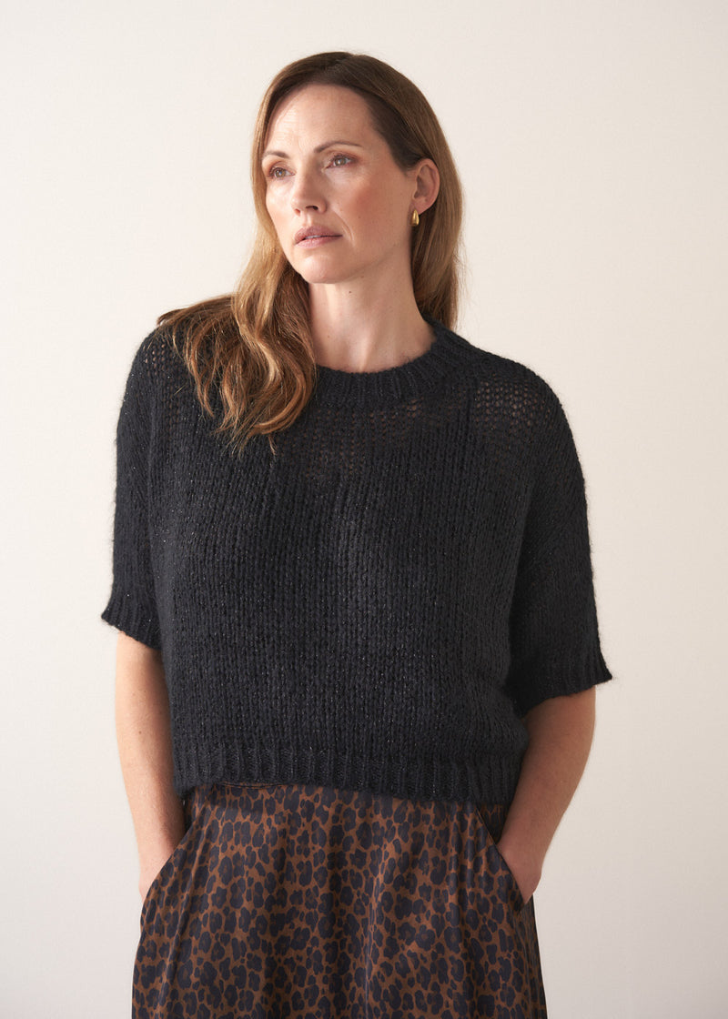 Woman wearing a black sparkle knit short sleeve sweater and a leopard print skirt on a plain background