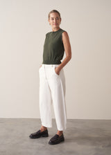 Woman wearing dark green fine knit sweater with removable heart brooch with white barrel leg jeans