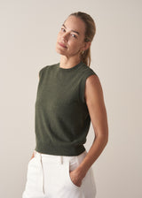 Woman wearing dark green fine knit sweater with removable heart brooch with white barrel leg jeans